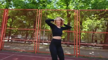Siyah spor kıyafetleri içinde fit bir kadın açık hava spor sahasında zıplama hareketi yapar. Fitness, sağlık ve refah.