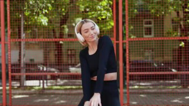 Yazın, açık hava basketbol sahasında siyah spor giyerek kulaklıklarıyla müzik eşliğinde dans eden genç bir kadın..