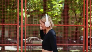 Spor kıyafetli bir kadın kulaklıkla müzik dinlerken mutlu bir şekilde dans eder..