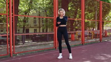 Kulaklık takan sportif bir kadın ısınıyor, fitness seansına hazırlanıyor. Telefonundan müzik dinliyor..