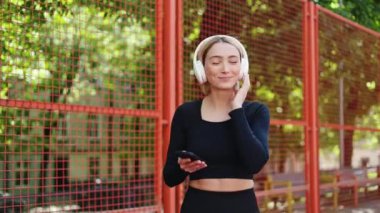 Genç sportif kadın kulaklıkla müzik dinliyor ve kameraya gülümsüyor..