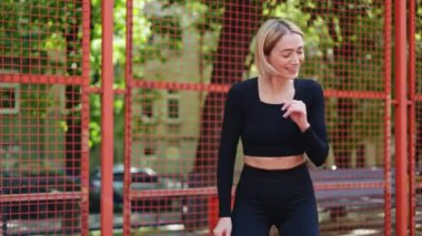 Siyah spor kıyafetli genç sarışın kadın sahada mutlu dans ediyor.