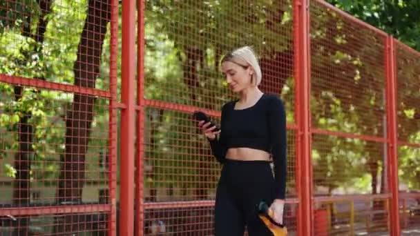 幸せなフィット感の女性は 運動後に休息の瞬間を楽しんで彼女の携帯電話をチェック — ストック動画