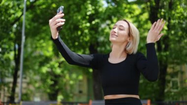 Genç ve zinde bir kadın parkta telefonuyla video görüşmesi yapıyor. Mutlu ve gülümsüyor..