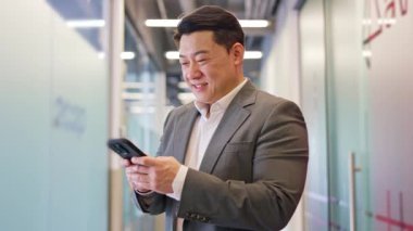 Elinde kablosuz akıllı telefon tutan komik bir erkek ve içeride sosyal medyayı kaydırıyor. Ofis içi cihaz kullanırken gülümseyen işadamı olumlu duygularını dile getiriyor..