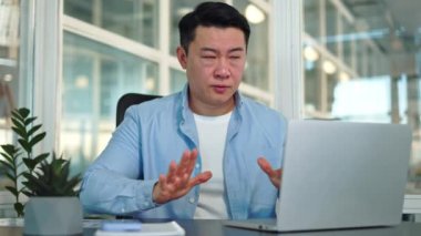 Sinirli Japon erkek ofisteki portatif dizüstü bilgisayarın önünde otururken nefes almaya çalışıyor. Kederli genç işçi panik atak geçiriyor ve elleri sallayarak ısıyı düşürüyor..