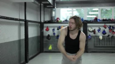 Spor kıyafetleri içinde şişmiş bir adam sıkıca sarılmış elleriyle dairesel hareketler yapıyor ve sırt ve gövde kaslarını geriyor. Profesyonel dövüşçü içeride yoğun dövüş antrenmanına başlamadan önce ısınıyor..