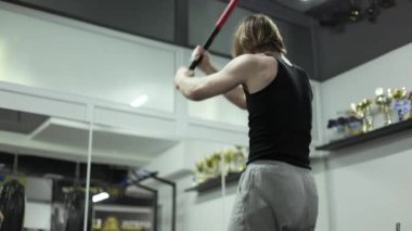 Stüdyoda ayna ve şampiyon fincanlarıyla ağır fitness çekiçiyle nesneyi yere vururken kolları ve sırtlarıyla çalışan zinde bir adam. Sporcu antrenman sırasında güç ve güç gösteriyor..