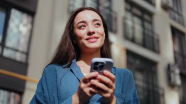 Güneşli bir günde genç bir kadın telefonuna bakarken gülümsüyor.