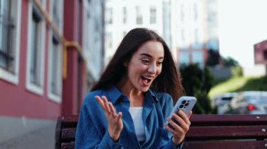 Bençte oturan kadının cep telefonuna duygusal tepkisi var.