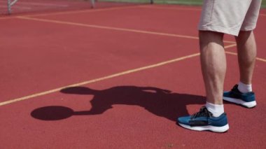 Turuncu sahanın ortasında dinamik aktif erkek basketbolunun yan görüntüsü. Mavi spor ayakkabıları konusunda yetenekli bir genç oyuncu. Yaklaşan yarışmaya hazırlanmak için açık havada antrenman yapıyor..