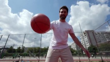 Dinamik genç adam turuncu sahanın ortasında basketbolu smaç basıyor. Beyaz tişört giyen aktif bir adam yarışmadan önce açık hava eğitimi alıyor. Egzersiz ve egzersiz kavramı.