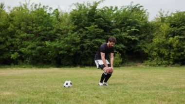 Kafkasyalı genç bir adam çimenli sahada, futbol topu yakınlarda. Şort giymiş ve siyah kollu gömlek giymiş bir erkek. Açık havada spor yapıyor. Futbolun spor ve spor.
