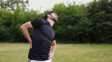 Kafkasyalı yaralı bir adam yeşil alanın ortasında duruyor ve sırtına masaj yaparken acı içinde kıvranıyor. Stresli insan omurilik krampıyla boğuşuyor ve terapi için antrenmanı yarıda kesiyor..