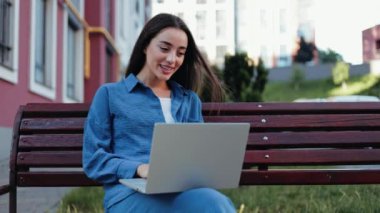 Genç bir iş kadını dışarıda bankta otururken bilgisayarında video konferansı yapıyor..