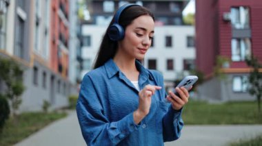 Mutlu genç kadın telefonuyla müzik dinliyor ve açık havada ritimle dans ediyor..