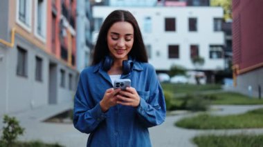 Şehirde kulaklık takıp akıllı telefon kullanan mutlu bir kadın..