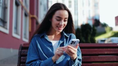 Mutlu genç kadın dışarıda akıllı telefondan sosyal medyada geziniyor.