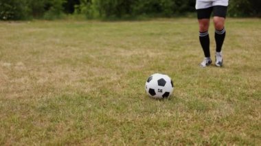 Enerjik bir adam spor kıyafetleri içinde geniş çimenlik alanda koşuşturuyor ve ayağıyla ustalıkla futbol topu sürüyor. Uzman bir sporcu açık havada sıkı bir antrenman yapıyor..