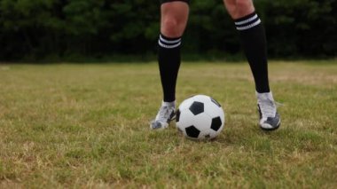 Siyah uzun çoraplar ve beyaz spor ayakkabılar giyip geniş çimlerde futbol topunun etrafında zıplayan aktif erkek bacaklarını kapatın. Yetenekli bir sporcu, temiz hava teçhizatıyla egzersiz yapıyor..