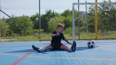 Çalışkan sporcu vücut pozisyonunu değiştiriyor ısınmak için bacakları yana eğiyor ve kaslarını esnetiyor. Sorumlu çocuk antrenman sırasında yaralanmaları önlemek için fiziksel uygulamalar kullanıyor.