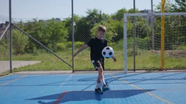 Beyazlı okul çocuğu topu takip ediyor ve oturma alanındaki stadyumda havaya fırlattığı için tekmeliyor. Futbol takımının hırslı kalecisi maçtan önce küçükler için rakip ligle ısınıyor..