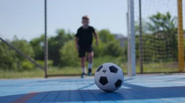 Sıska çocuk topa vurmaya hazırlanıyor, topa koşuyor, tepeye ayak basıyor ve ağlarla çevrili açık stadyumda ilerliyor. Yerel futbol takımına katılmak için spor disiplini konusunda aktif çocuk eğitimi.