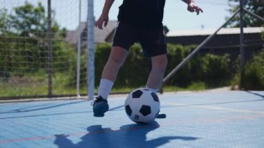 Kesilmiş okul çocuğu futbol topuyla manevra yapıyor ve bir kapıdan diğerine futbol sahasının ortasına gidiyor. Aktif akademi öğrencileri yaz boyunca ek beden eğitimi dersleri alıyorlar..