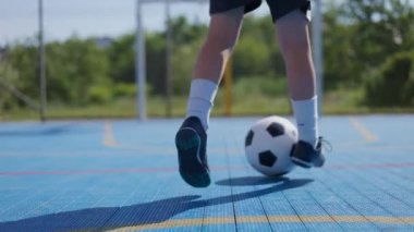 Futbol topuyla oynarken siyah şortlu, siyah çizmeli beyaz bir çocuğun bacakları kesilmiş. Futbolcu açık hava sahasındaki antrenman sırasında top sürüyor ve kapıya doğru ilerliyor..