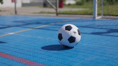 Futbol topunu, bilinmeyen biri tarafından tekmelenen kırmızı ve sarı işaretli mavi kapaklı oyun alanına yakın tut. Koşan uzun çoraplı bir çocuk futbol maçında takım arkadaşına pas veriyor..