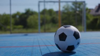 Futbol topunun mavi kort yüzeyine yerleştirilmesi ve profesyonel spor ayakkabılarda erkek çocuk tarafından tekmelenmesi. Futbol akademisi öğrencisi boş kapılarda oyun ve gol atma aracı.