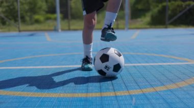 Siyah-beyaz futbol topunu kapat, uzun beyaz çoraplı ve profesyonel ayakkabılı tanınmayan biri tarafından tekmeleniyor. Atletik adam sarı işaretli mavi yüzeyde becerilerini geliştiriyor..