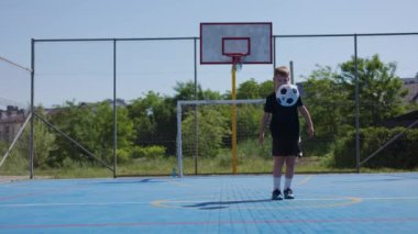 Sarışın okul çocuğu futbol topunu havaya fırlatıyor ve bacağıyla birkaç kez dışarı doğru tekmeliyor. Atletik genç beden eğitimi dersinde doğruluk ve konsantrasyon pratiği yapıyor..