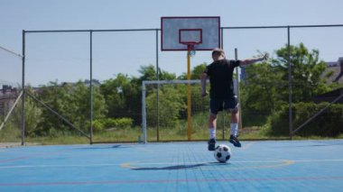 Sıcak yaz günü mavi kaymayan yüzeyi olan, spor sahasında futbol antrenmanı yapan çalışkan bir çocuk. Takım üniformalı genç futbolcu siyah beyaz top etrafında daireler çiziyor..