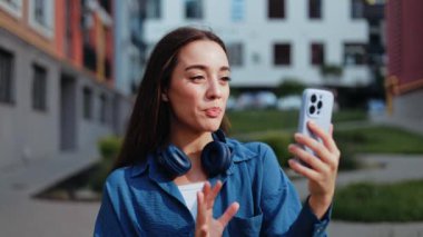 Dışarıda yürürken telefonunu kullanan mutlu genç bir kadın.