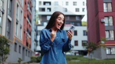 Heyecanlı genç kadın, akıllı telefonundan iyi haberler okuduktan sonra kutlama yapıyor.