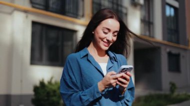 Şehirde gülümseyen genç bir kadın telefonunu karıştırıyor. Telefondaki iş kadını..