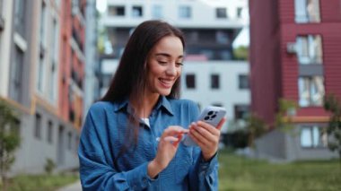 Açık havada akıllı telefon kullanan gülümseyen genç bir kadın. Şehir teknolojisi yaşam tarzı.
