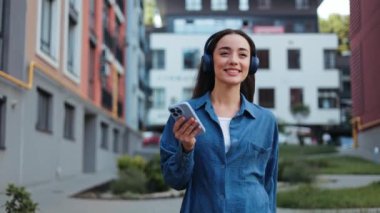 Kaygısız genç kadın telefonuyla müzik eşliğinde dans ediyor ve yürüyüş yapmaktan zevk alıyor..