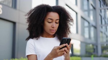 Açık renk elbiseli çekici bir kadın uzaktan gelen bir arkadaşından iyi haberle mesaj alırken akıllı telefon kullanıyor. İş bölgesinde yürürken posta kutusuna bakarken sevinen genç esmer..