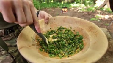 Eller taze otları ve baharatları dışarıda pişirmek için ahşap bir kasede karıştırıyor..