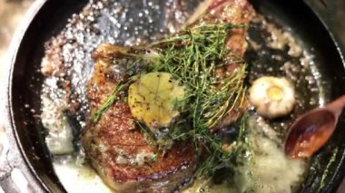 Sarımsak ve bitkisel tereyağının döküm demir bir tavada sıcak bifteğin üzerine dökülüşünü kapat.