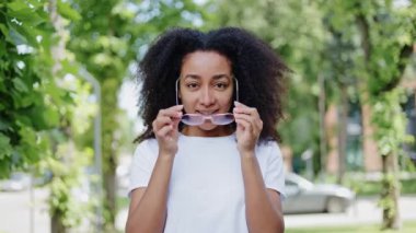 Çekici Afro-Amerikan kadın portresi ağaçların yanına gidiyor ve açık havada gözlük takıyor. Sıradan beyaz tişörtler giymiş olumlu genç bir kadın doğrudan hoş duygularla bakıyor..