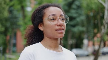 Yeşilliğin arka planında dikilirken gözlüklü neşeli kadının portresini yakından çek. Pozitif ifade eden ofis ekipmanlarıyla Afro-Amerikan kadın..