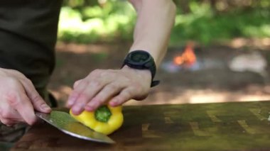 Tahta kesme tahtasının üzerinde sarı dolma biber dilimleyen birinin yakın plan fotoğrafı..