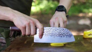 Bir şefin, açık havada ahşap bir kesme tahtasındaki sarı dolma biberi ustalıkla doğradığı yakın çekim.