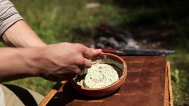 Bir adamın ellerinin açık havada malzemeleri karıştırdığı yakın çekim. Doğal ortamdaki bir yemeğin hazırlanmasını vurguluyor..