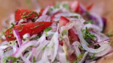 Tahta kaşık kırmızı soğan, domates ve otlardan oluşan taze ve canlı bir salatayı kırsal bir kaseye atıyor.