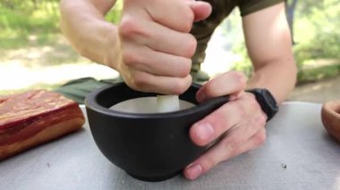 Açık havada domuz pastırması pişirmeye hazırlanmak için havan ve tokmak kullanarak karabiberi ince bir toza dönüştüren birini yakından çek.