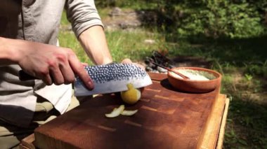 Bir insanın ellerinin, doğadaki ahşap kesim tahtasındaki bir bıçakla limonu dikkatlice keserken yakın çekim görüntüsü..